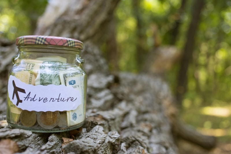 Jar of money labeled with Adventure sitting on a log in the woods