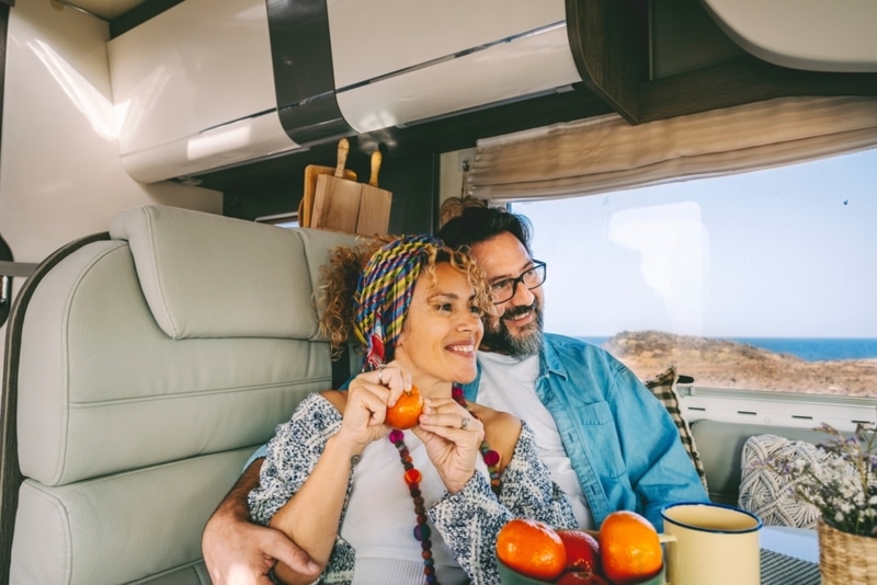 Cheerful mature couple smile and hug sitting inside camper van