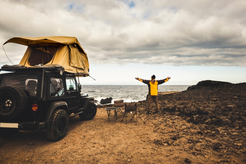 Man looking at the ocean next to his Jeep with a rooftop tent